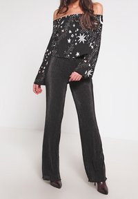 Top negro sin hombros con patrones de estrellas en plata y dorado; combinado con pantalones de pierna ancha plisados negros de cintura alta y tacones puntiagudos.