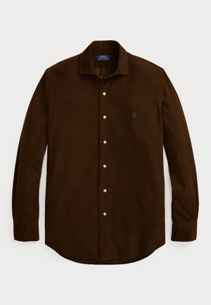 Chemise à boutons marron en velours côtelé avec des manches longues, un col et un petit logo vert sur la poitrine gauche. Huit boutons sur le devant.