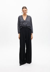 Sivý pletený cardigan s hlbokým výstrihom do V a gombíkovým zapínaním. Vhodný s čiernymi širokými nohavicami s vysokým pásom. Hladká textura; bez vzorov.