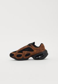 Chaussure Nike avec un dessus en suede marron et des accents en maille noire. Forme arrondie, semelle avec coussin d'air visible, et motif découpé unique sur les côtés.
