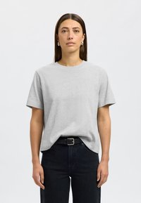 Sivé bavlnené tričko s krátkymi rukávmi, okrúhlym výstrihom a vo voľnom strihu. Nosí sa s čiernymi džínami s vysokým pásom a čiernym pásom. Hladká textúra.