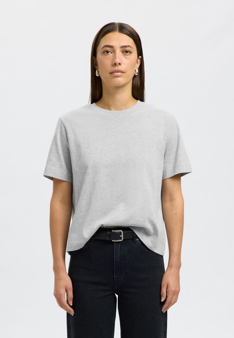 Sivé bavlnené tričko s krátkymi rukávmi, okrúhlym výstrihom a vo voľnom strihu. Nosí sa s čiernymi džínami s vysokým pásom a čiernym pásom. Hladká textúra.