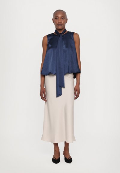 Navy satin sleeveless top with a neck tie, paired with a light beige, ankle-length skirt and black pointed flats. Smooth texture throughout.