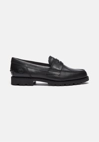 Mocassin penny en cuir noir avec semelle crantée et logo embossé sur le talon, présenté sur fond blanc.
