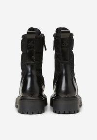 Černé boty s prošívanou textilní svrchní částí a lesklým koženým podpatkem. Mají boční zip a odolnou gumovou podrážku s hlubokými drážkami.