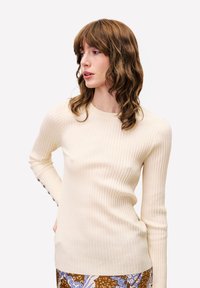 Lichtcrème geribbeld sweater met lange mouwen, ronde halslijn en knoopaccenten op de manchetten. Glad textuur, een aansluitend ontwerp.
