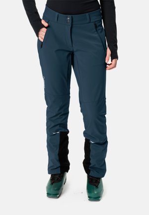 Pantaloni da sci blu navy con texture liscia, due tasche laterali, gambe inferiori nere rinforzate e cintura regolabile, abbinati a scarponi da sci verdi.