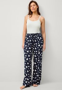 Top sin mangas blanco con encaje, combinado con pantalones de pijama azul marino con patrones de corazones blancos; tela suave, corte holgado y cinturilla elástica.
