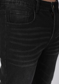 Μαύρα τζιν από τζιν ύφασμα με στενή γραμμή, διακοσμημένα με διακριτική αποχρωμάτωση, κλασικό σχέδιο με πέντε τσέπες και κλείσιμο με μεταλλικό κουμπί. Λείο ύφασμα.