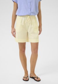 Light yellow shorts with an elastic waistband and drawstring. Made of a soft, textured fabric. Paired with a short-sleeved blue button-up shirt.