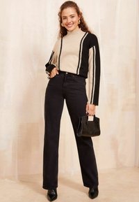 Maglione a strisce beige e nere con maniche lunghe, collo alto, abbinato a jeans neri a zampa e una piccola borsa nera.