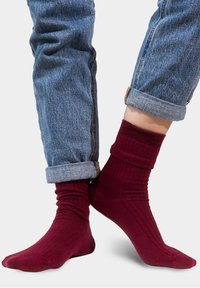 Bordowe skarpetki w prążki wyeksponowane obok zwiniętych jasnoniebieskich spodni dżinsowych, charakteryzujących się gładką teksturą i dopasowaniem wokół kostek.