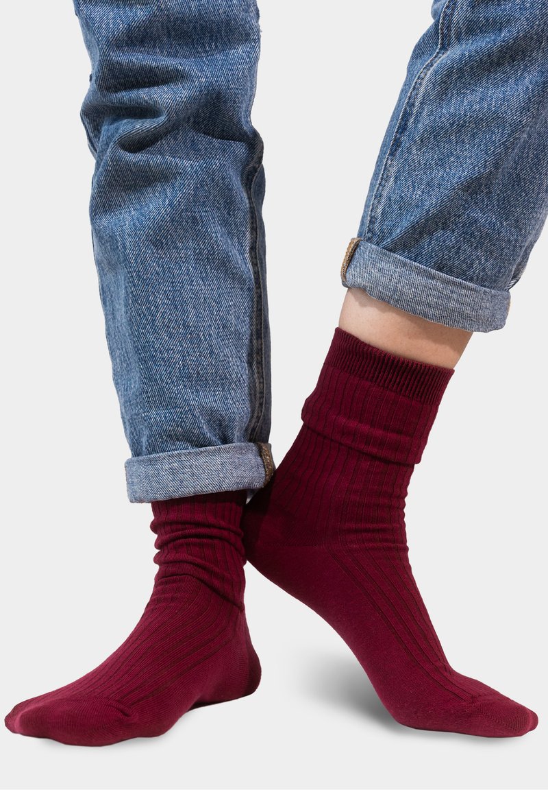 Bordowe skarpetki w prążki wyeksponowane obok zwiniętych jasnoniebieskich spodni dżinsowych, charakteryzujących się gładką teksturą i dopasowaniem wokół kostek.