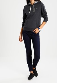 Donkergrijze hoodie met lichtgrijze voering, witte koordjes en voorzak. Gekocht met marineblauwe jeans en zwarte sneakers. Eenvoudig ontwerp.