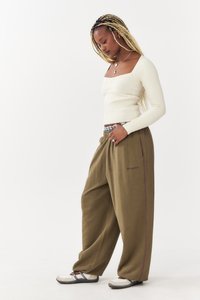 Haut crème à manches longues à nervures avec décolleté carré, associé à un pantalon ample vert olive avec une bande latérale violette et un logo brodé.