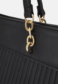 Close-up of black handbag with vertical ribbed texture, leather straps, and gold chain links connecting straps to bag.