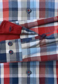 Nahaufnahme eines gefalteten Karoshirts mit roten, blauen, weißen und grauen Karos, ausgestattet mit blauen Knöpfen und roten Fadendetails.