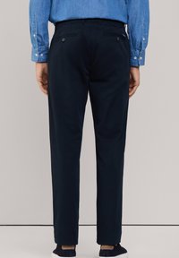 Marineblauwe broek met een recht model, voorzien van achterzakken met knoopsluitingen, gemaakt van een soepele stof. G gedragen met een denim overhemd.