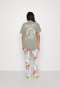 Grå oversized t-shirt med tryckt design av kokosnötskartong; kombinerad med färgglada, mönstrade byxor med olika tropiska motiv. Gröna sandaler.