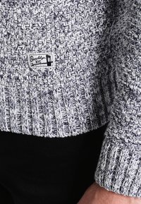 Sweter dziergany w kolorze granatowym i białym, z fakturowanym wzorem, prążkowanym dołem oraz metką z napisem "Brooklyn NYC".