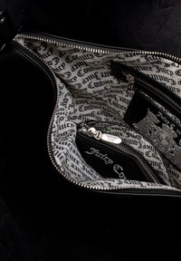 Interno di una borsa nera con cerniere. Foderato con un tessuto bianco con stampa nera ripetuta. Include una piccola pochette e accenti in metallo lucido.