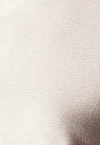 Cremefarbener Strickstoff mit glatter Textur und dezentem horizontalem Rippenmuster, das die weichen und atmungsaktiven Eigenschaften betont.