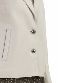 Crème leren blazer met een matte afwerking, voorzien van een notch-kraag, dubbele knoopsluiting en zwarte plastic knopen.