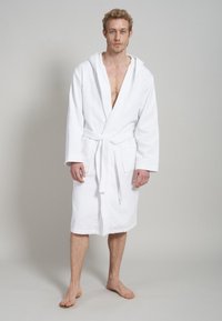 White terry cloth bathrobe with a hood, waist tie, and two front pockets. The fabric has a soft texture and is knee-length.
