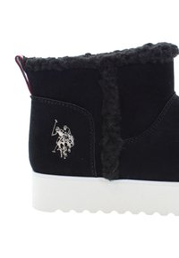 Schwarze Knöchelstiefel mit weichem Besatz, weißer Sohle und kleinem silbernen Polo-Spieler-Emblem an der Seite.