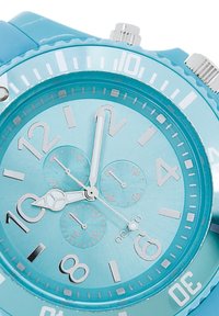Une montre-bracelet en plastique turquoise avec un cadran rond, des marqueurs d'heure blancs, trois sous-cadrans et des aiguilles argentées. Cadran texturé avec des marqueurs de 30 minutes.