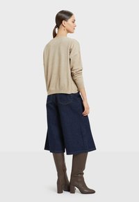 Beige sweater with long sleeves, paired with dark blue wide-leg denim skirt, and brown knee-high block-heel boots. Plain background.