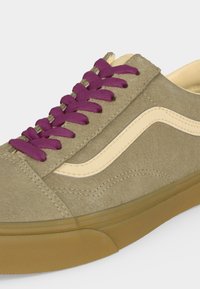 Baskets en daim beige avec lacets violets, bande latérale blanche et semelle en gomme sur fond blanc.