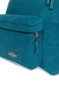 Mochila de forro polar en color verde azulado que cuenta con un bolsillo frontal con cremaller y una superficie texturizada, además de un parche con el logotipo de Eastpak sobre una base rectangular.