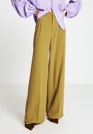 Weit geschnittene Hosen aus senfgelbem Stoff, mit einer taillierten hohen Taille und glatter Textur; kombiniert mit spitzen olivgrünen Absätzen.