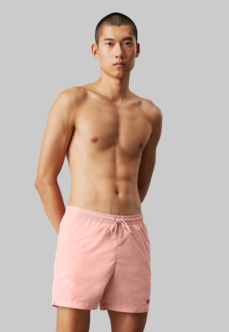 Shorts da bagno rosa chiaro realizzati in tessuto morbido, dotati di una vita elastica con cordoncino, tasche laterali e un piccolo dettaglio con logo.