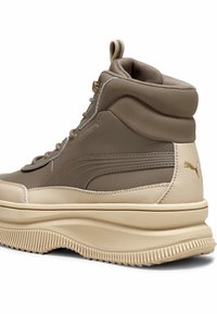 Zapatillas altas marrón y beige con cuero texturizado, suela acanalada y detalles en dorado. Cuenta con un tobillo acolchado y una pestaña en la parte trasera.
