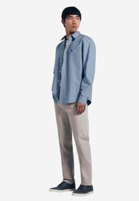 Camicia azzurro chiaro con bottoni e maniche lunghe, pantaloni beige e sneakers scure. La camicia ha una tasca sul petto e una vestibilità comoda.