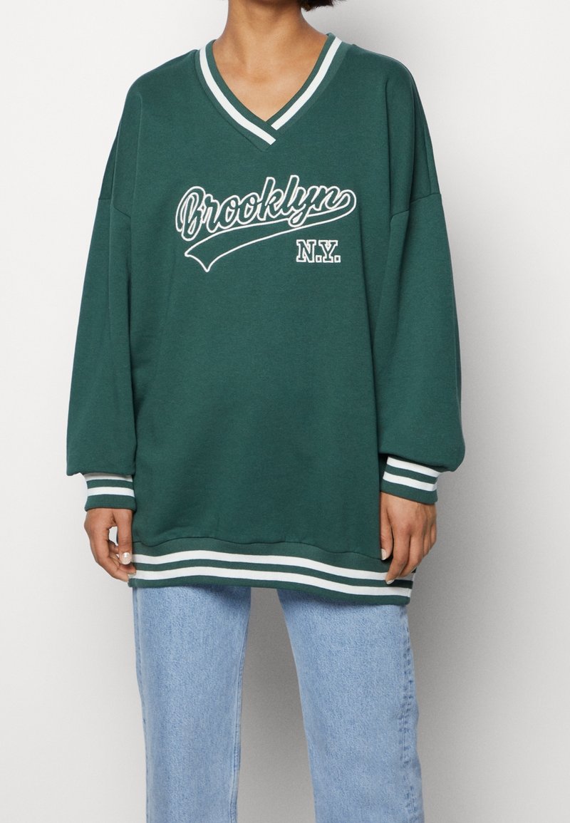 Sweatshirt vert surdimensionné avec un graphisme blanc Brooklyn et N.Y. ; possède un col en V, des poignets rayés et un ourlet.