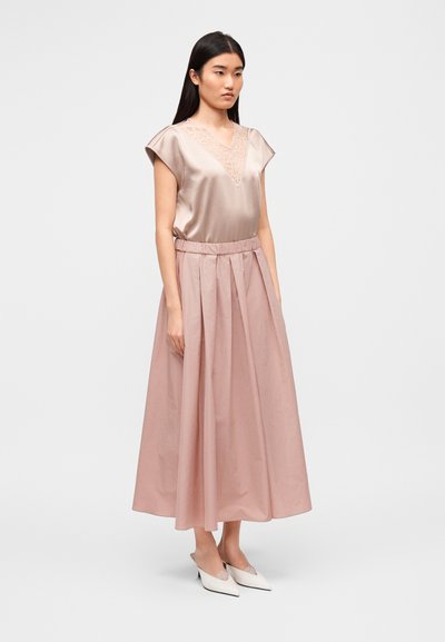 Σατέν τοπ σε ροδακινί απόχρωση με διακοσμητικό δαντελένιο ντεκολτέ σε σχήμα V, συνδυασμένο με μακριά, πλισέ φούστα σε ροδακινί απόχρωση με ελαστική μέση. Απλά λευκά mule παπούτσια.