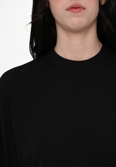 Haut noir à col montant avec une texture lisse et une coupe décontractée. Présente un design uni sans motifs ni ornements.