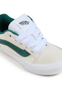 Baskets blanches et vertes avec un dessus en daim et toile, bout rond, lacets épais et un logo noir sur la languette.