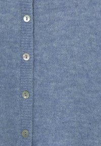 Cárdigan de punto azul claro con seis botones redondos y brillantes y una superficie texturizada. Presenta bordes acanalados a lo largo de la tapeta de botones.