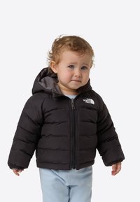 Czarna kurtka puchowa z kapturem, z poziomym przeszyciem i srebrnym zamkiem błyskawicznym. Noszona na jasnoniebieskich spodniach z detalem logo.