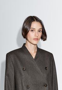 Dvojřadový šedý vlněný blazer s kulatými tmavými knoflíky a zářezovým límcem, nabízející přiléhavý střih a hladkou texturu.