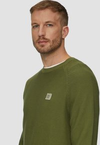 Pull vert en maille textur�ée. Doté d'un col rond et d'un petit patch logo sur la poitrine. Design simple et ajusté.