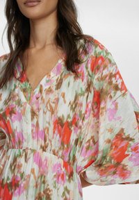Rochie florală multicoloră dintr-un material ușor, cu decolteu în V, mâneci largi și talie gathered. Prezintă nuanțe de roz, roșu și verde.