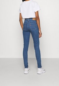 Jeans de mezclilla azul de corte ajustado con una cintura de altura media, que cuentan con un parche de cuero en la parte trasera, doble bolsillo trasero y detalles de costura sutiles.