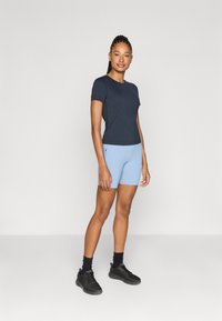 Marineblå t-skjorte med kort erm, kombinert med lyseblå shorts og svarte joggesko. Plaggene har en tettsittende design og minimalistisk stil.