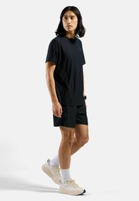 Zwart T-shirt met korte mouwen, gecombineerd met zwarte shorts. Model draagt lichtgekleurde sneakers en witte crew-sokken. Eenvoudig, atletisch ontwerp.