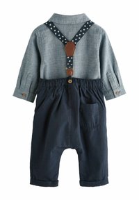 Blaues Hemd mit Kragen und Knopfmanschetten, kombiniert mit dunkelblauen karierten Latzhosen. Mit sternmustergeprägten verstellbaren Hosenträgern und einer Tasche.